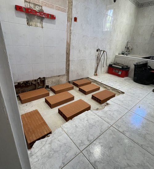 Intervention plombier Klimpec : briques creuses disposées au sol pour caler et stabiliser un bac de douche lors de la pose.